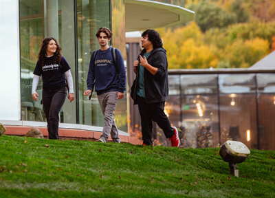 Three students walk behind the glass windows of the Arnold Bernhard Library