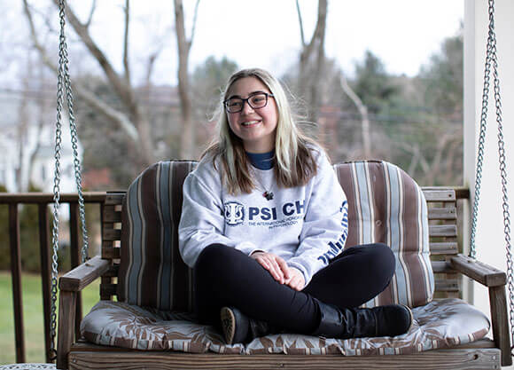 Nicole Antaya sits outside on a porch swing with her legs crossed under her.