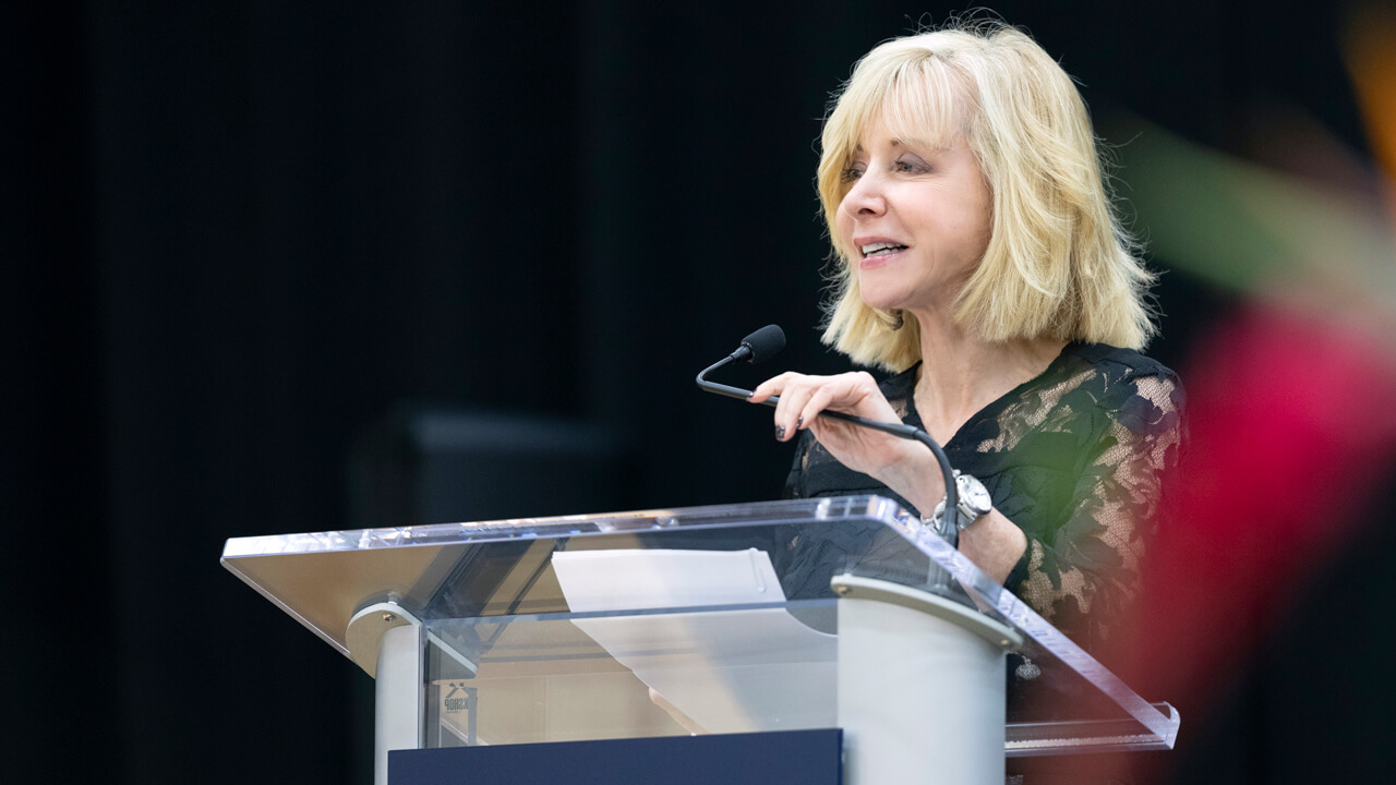 Quinnipiac President Olian delivers a speech from behind a clear podium