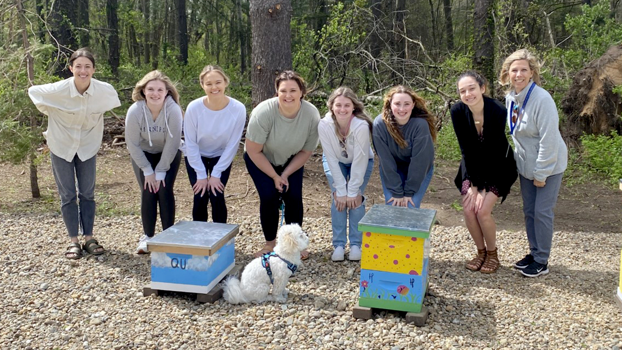 A group of students stand in front of decorated bee hives