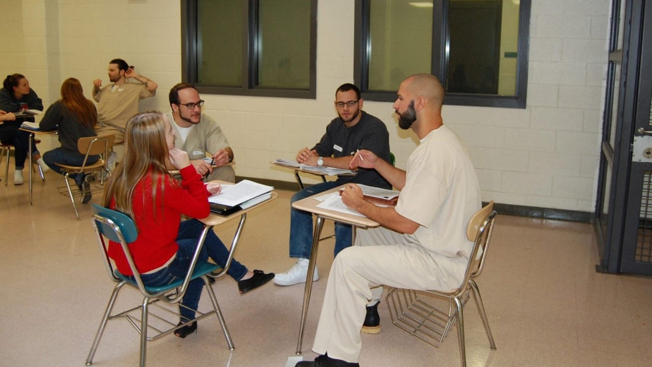 Criminal justice students work with an inmate in a classroom setting at a local prison