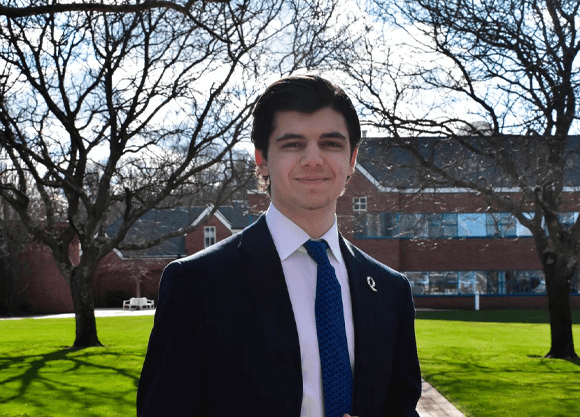 Student standing on Mount Carmel campus smiling at the camera in a suit.