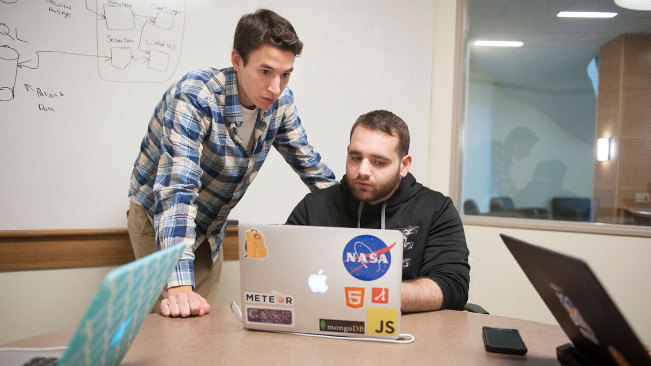 Two students looking at a laptop together in a room