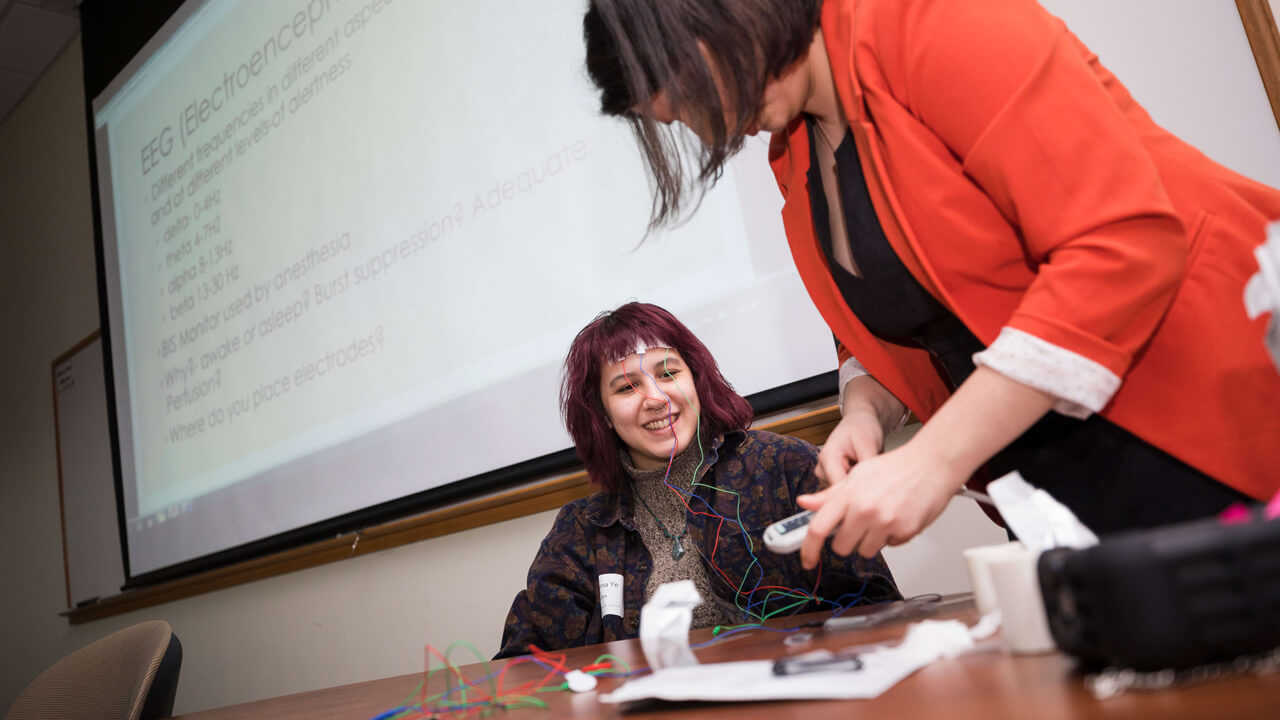 Student sits at desk with wires and sensors on her forehead during NEURON conference demonstration