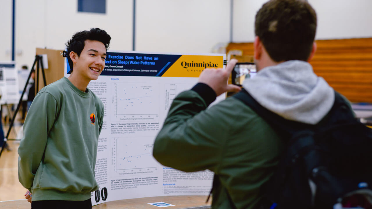 A student presents their poster project to a fellow classmate.