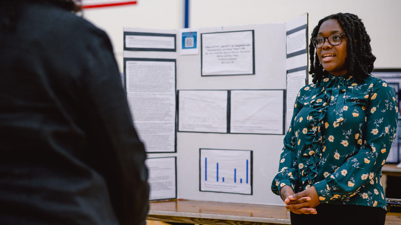 A student presents their poster project to a fellow classmate.