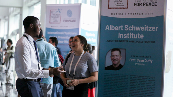 Two people talk at world summit day at the ASI table.