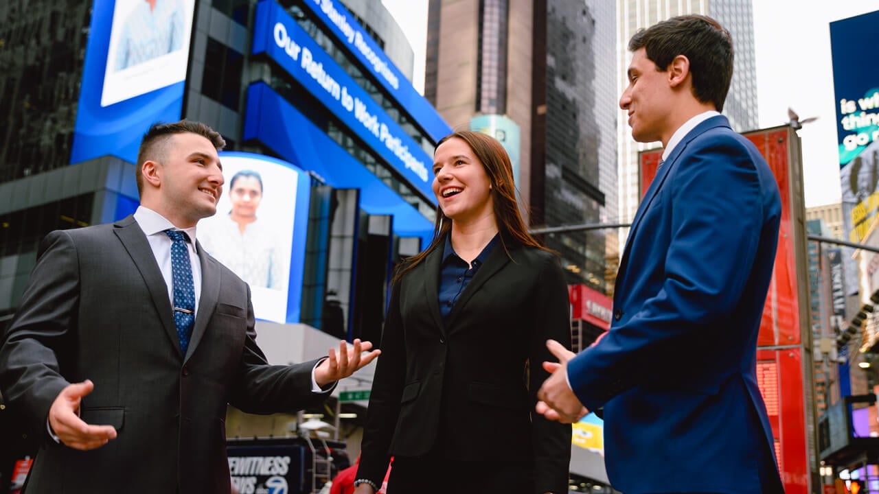 2 male students and a female student speaking to each other outside in NYC