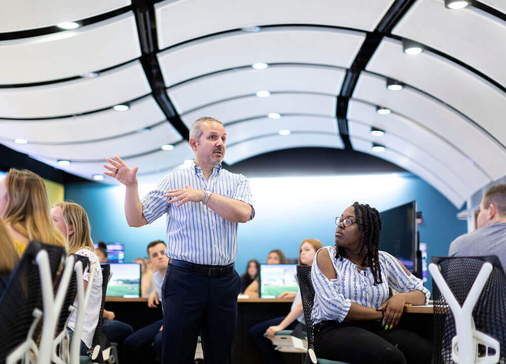 A finance professor speaks to a class of students in the Financial Technology Center on the Mount Carmel Campus