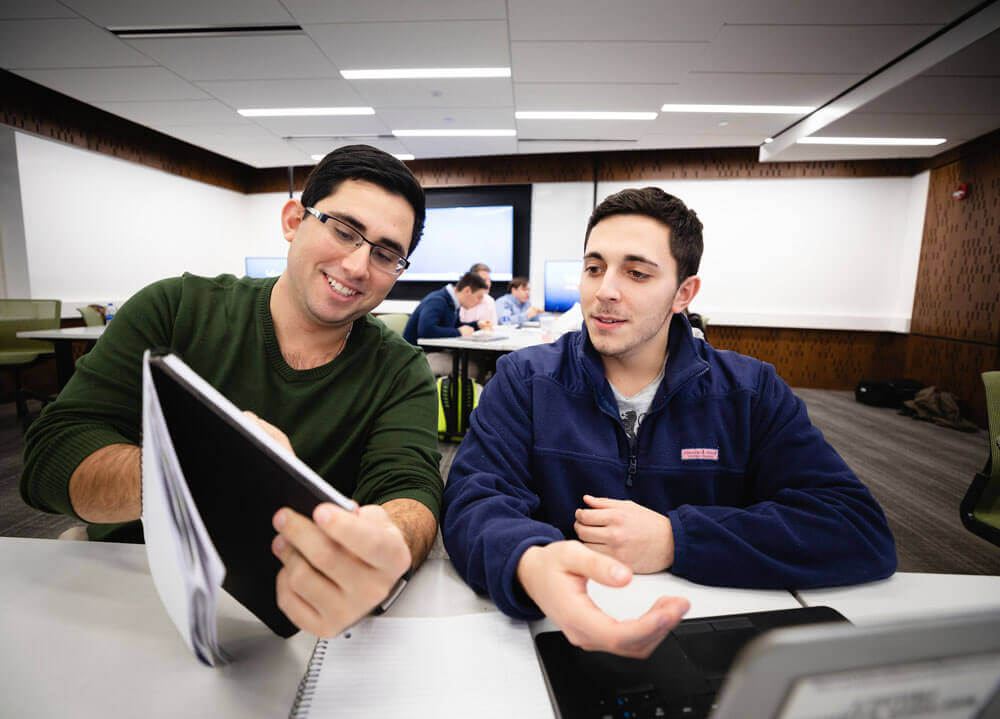 Two students sitting together while looking at a book