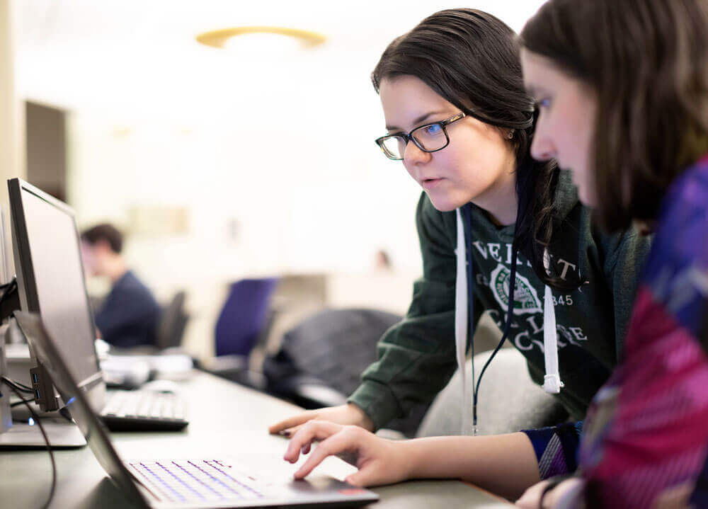 Two students look at a computer in the Arnold Bernhard library