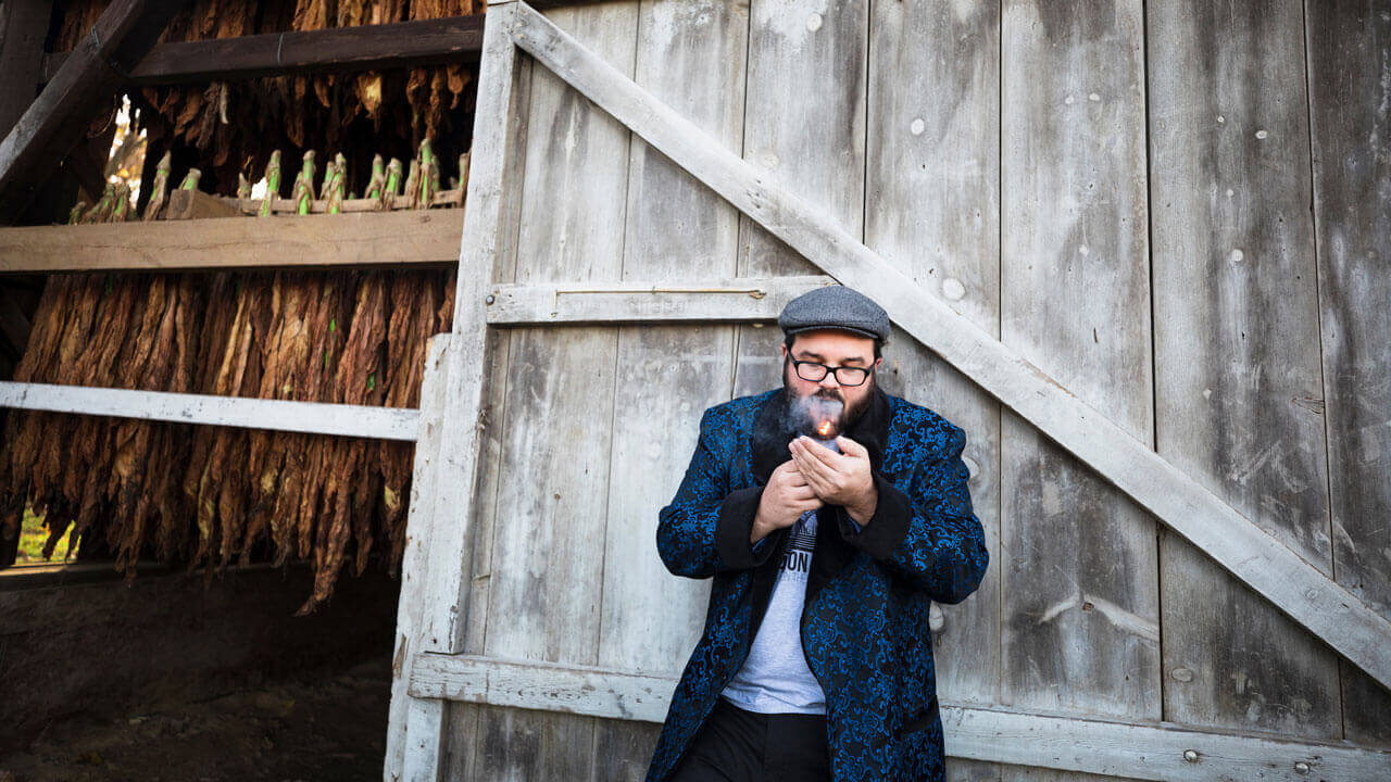 Nicholas Melillo lights a cigar in front of one of his tobacco barns