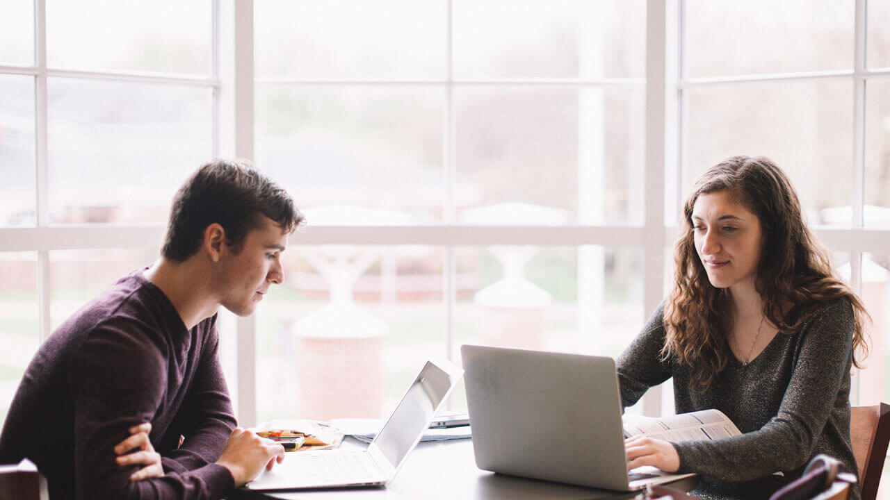 wo students studying together with the Lender School of Business in the background.