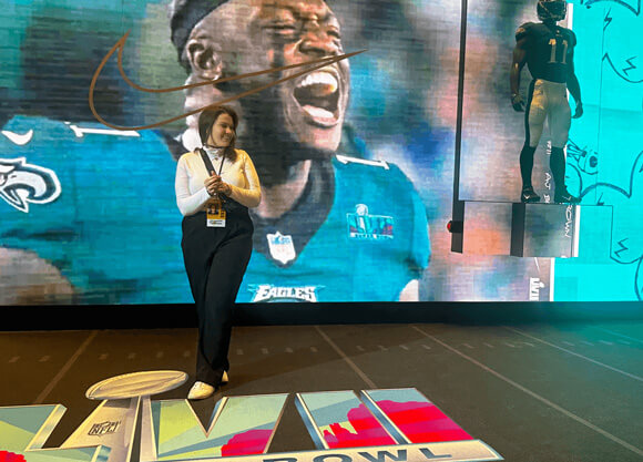 Carly MacManus poses in front of an interactive experience of screens at Super Bowl LVII press week.