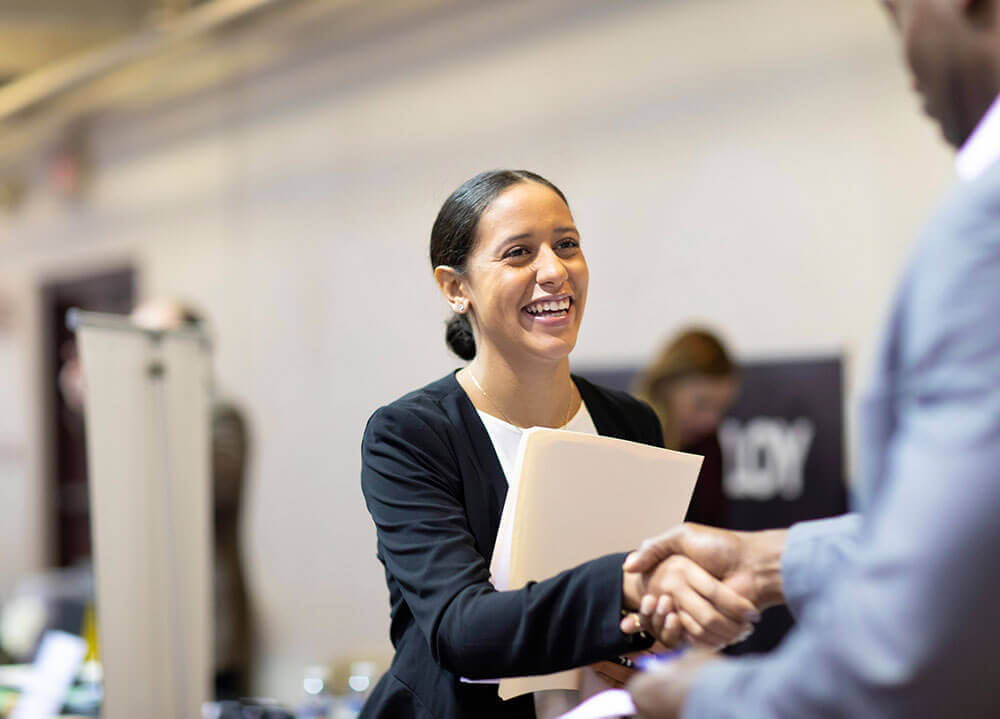 A public relations students shakes the hand of a potential employer at a career fair held on campus