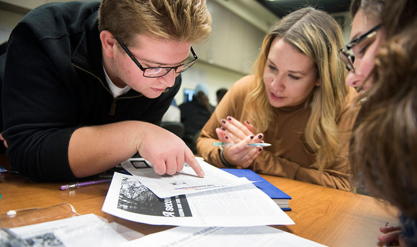 Three communications students wearing glasses go over edits to the student newspaper