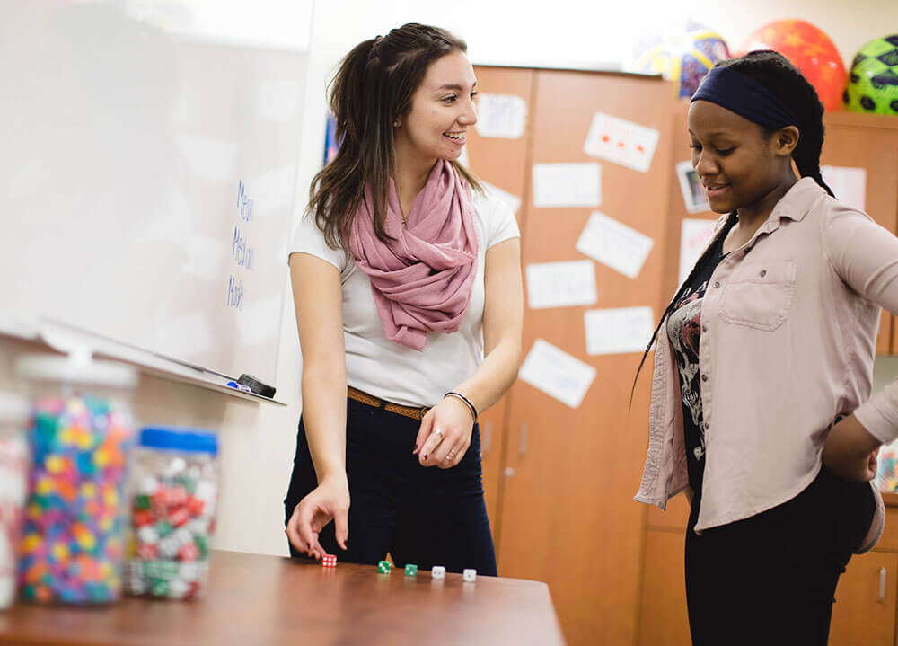 A School of Education student plays a dice game with a high school student on the North Haven Campus