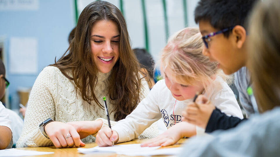 A School of Education student works with elementary schoolers on coursework at their desks