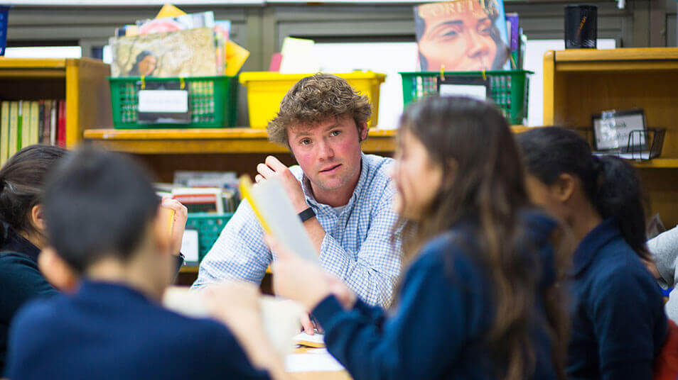 A School of Education student sits in a circle with a group of elementary school students