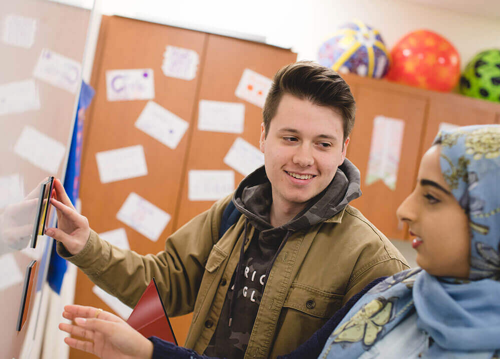 Two education students work on a lesson plan together by writing on a white board