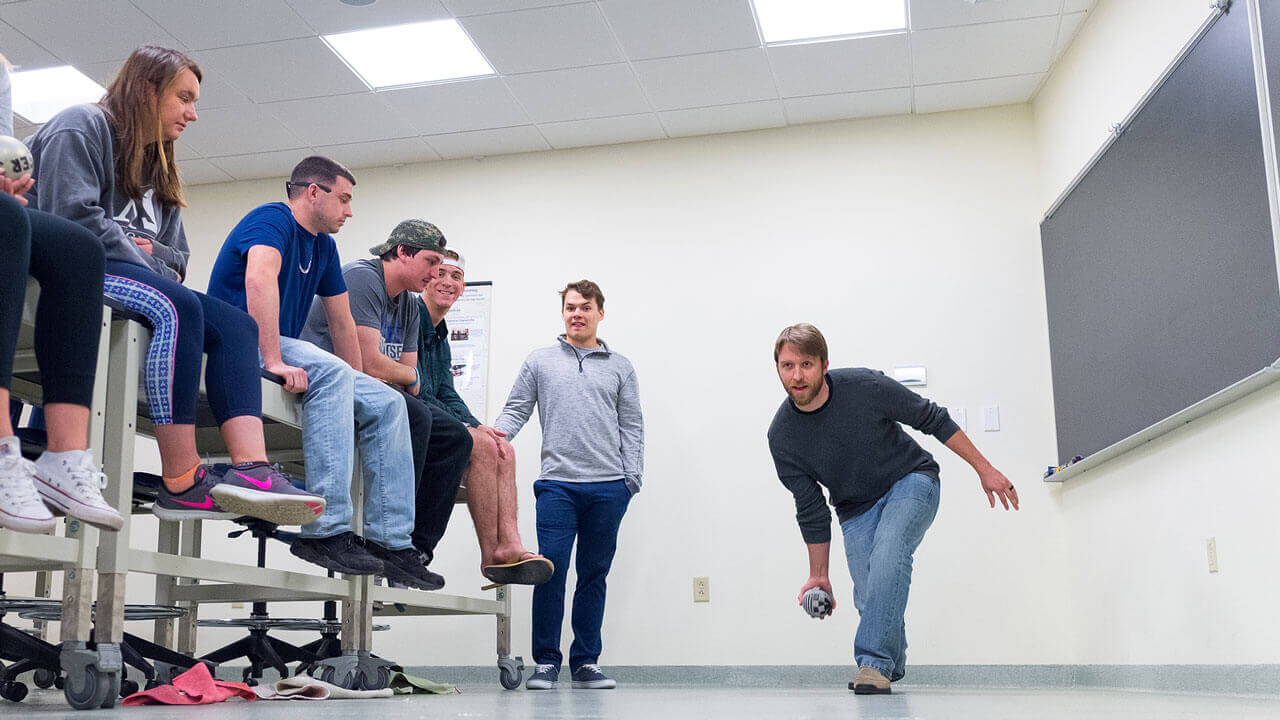 A student rolls a bowling ball in a classroom