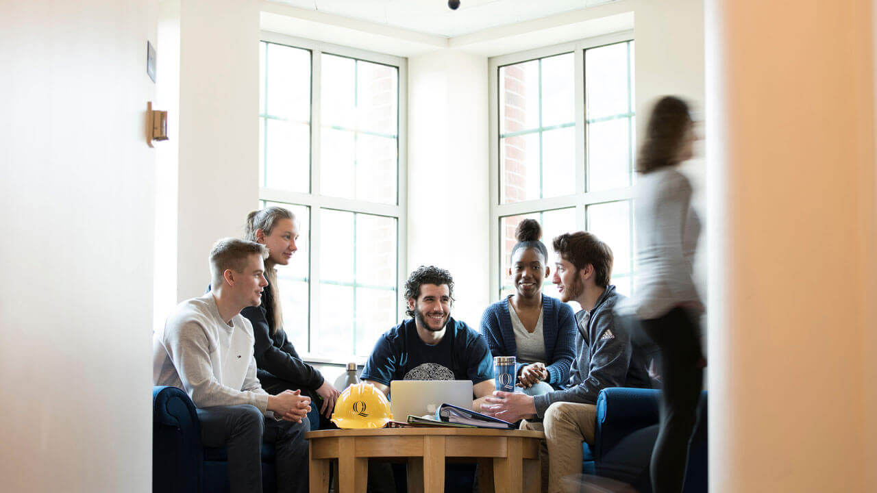 A group of students sit around a table talking to one another