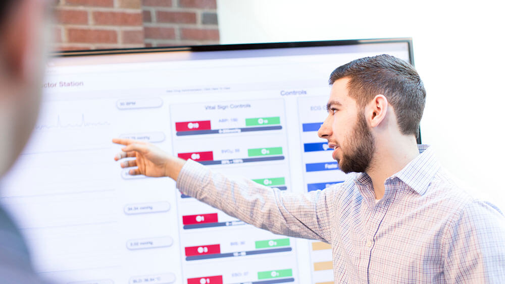 A software engineering student gestures toward a presentation on a big television screen