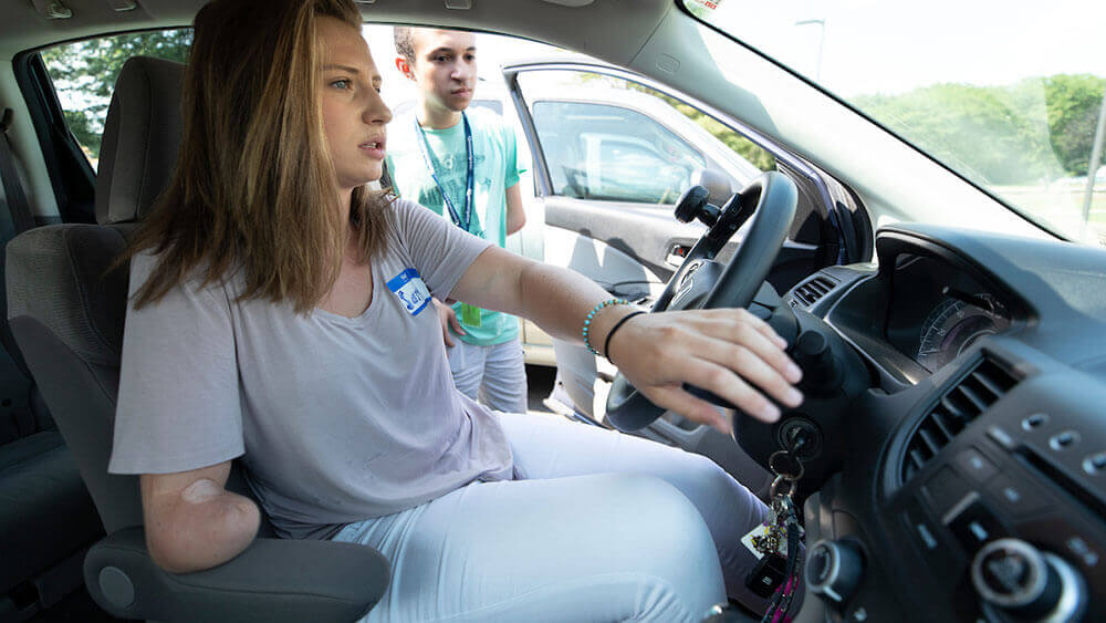 A young woman with limb loss steers a specially designed car