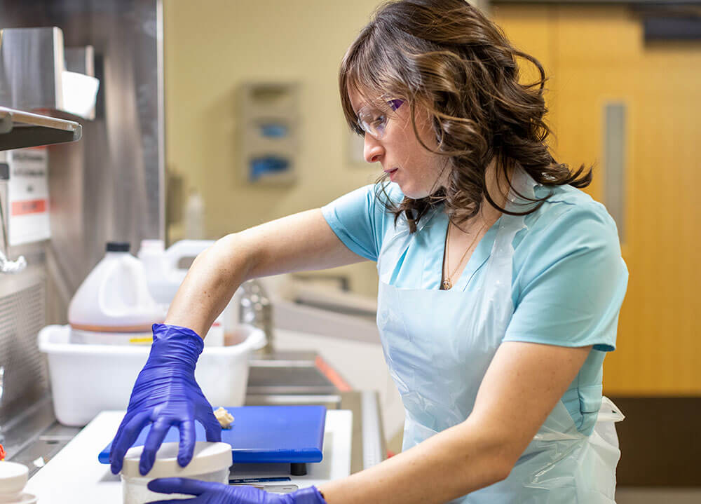 A health sciences student wearing safety glasses and gloves screws the cap on a specimen container in a laboratory