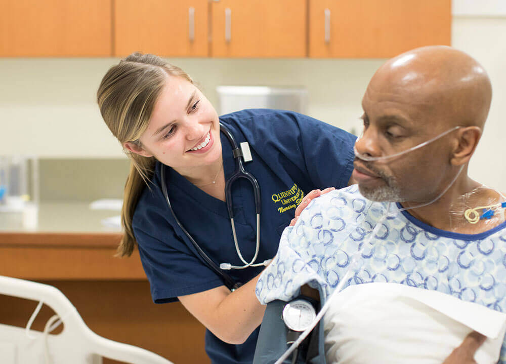 A nursing student smiles as she check on a patient during a simulation lab