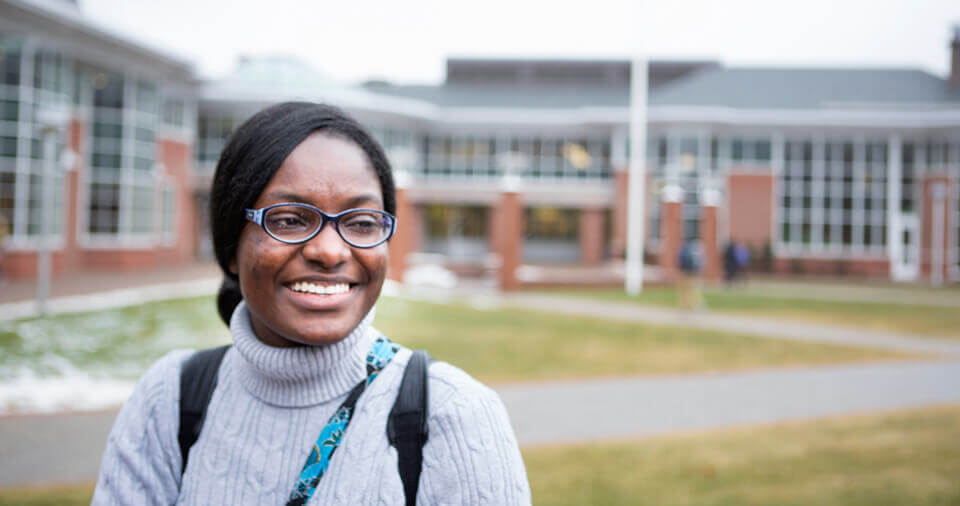 A transfer student wearing a backpack stands on the quad in front of the student center