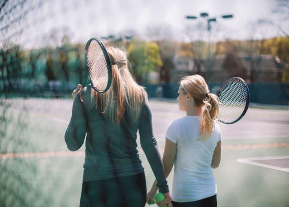 Two girls walking with tennis rackets in hand