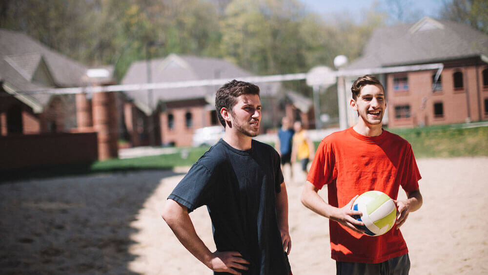 Students playing volleyball on the beach volleyball courts outside dormitories on the York Hill campus.