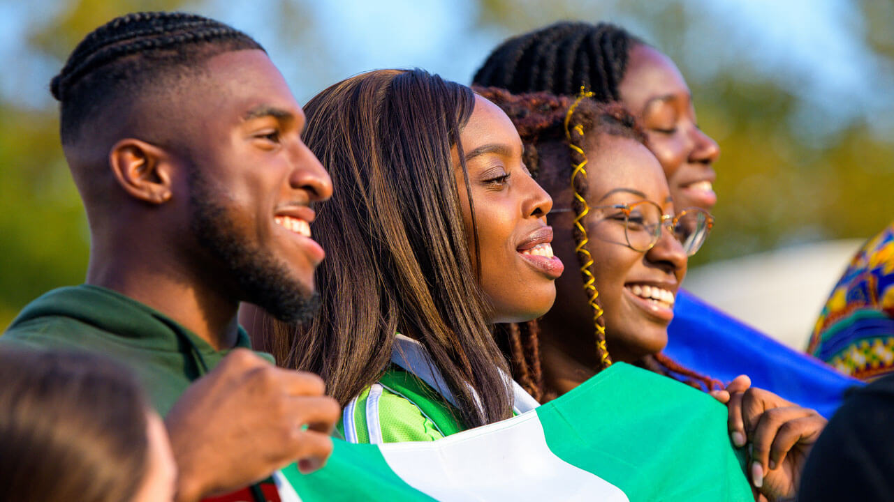 A group of international students hold flags from their country and smile together